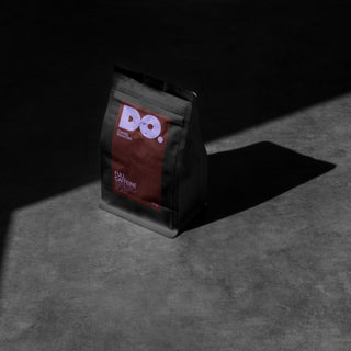 A sealed bag of Do Coffee Seasonal Espresso blend coffee beans on a shadowy surface.